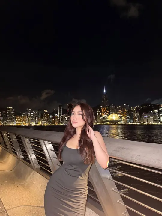 Debbie by a harbour at night, city lights behind.