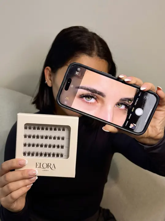 Selfie of a woman holding her phone and an Elora lash pack.